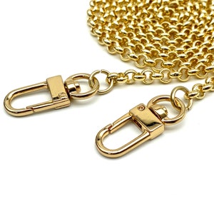 Op de afbeelding: Gouden ketting met twee gouden karabijnhaken. De ketting is opgerold en de karabijnhaken zijn open.