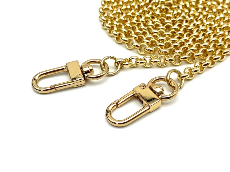 Op de afbeelding: Gouden ketting met twee gouden karabijnhaken. De ketting is opgerold en de karabijnhaken zijn open.