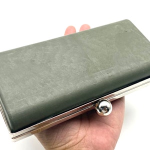 May include: A gray clutch purse with a silver metal frame and a silver clasp. The purse is closed and has a textured surface.