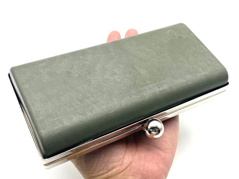 May include: A gray clutch purse with a silver metal frame and a silver clasp. The purse is closed and has a textured surface.