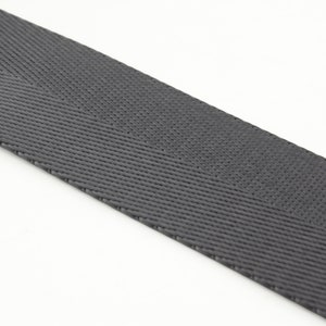 May include: A close-up of a gray woven webbing strap. The strap is made of a durable material and has a herringbone pattern.