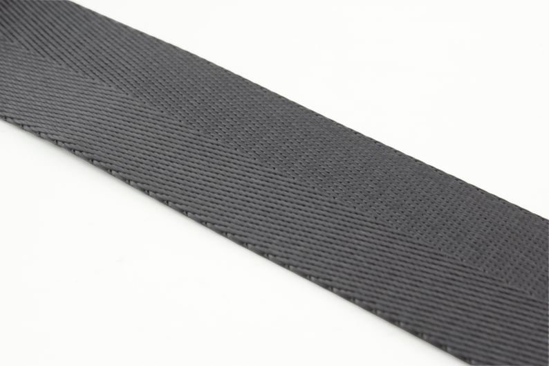 May include: A close-up of a gray woven webbing strap. The strap is made of a durable material and has a herringbone pattern.