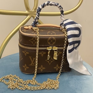 Op de afbeelding: Een bruine en beige monogram-handtas met een gouden kettingriem en een wit en blauw gepatroneerd stoffen handvat.