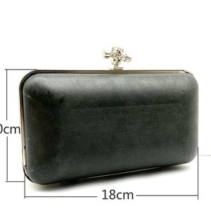May include: A black clutch purse with a silver clasp and a decorative knot detail. The purse measures 18 cm by 10 cm.