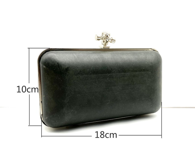 May include: A black clutch purse with a silver clasp and a decorative knot detail. The purse measures 18 cm by 10 cm.