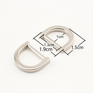 May include: Two silver metal D-rings with measurements in centimeters. The larger ring is 1.5 cm wide, 1 cm tall, and 1.3 cm deep. The smaller ring is 1.9 cm wide.