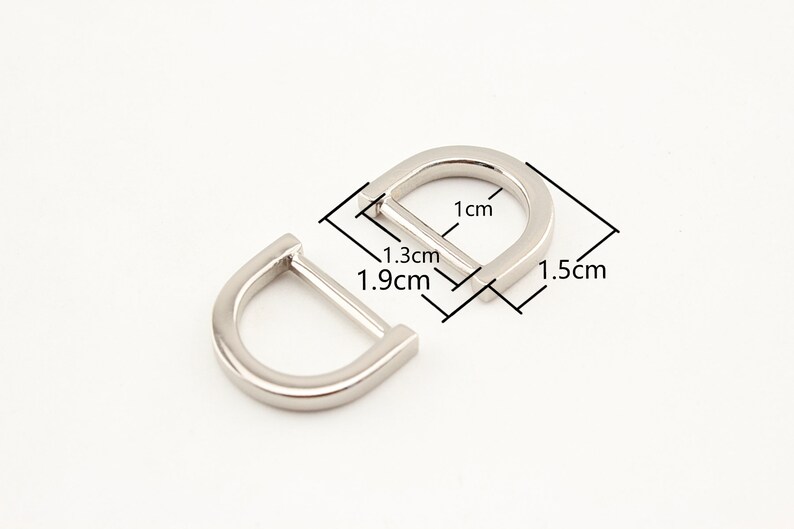 May include: Two silver metal D-rings with measurements in centimeters. The larger ring is 1.5 cm wide, 1 cm tall, and 1.3 cm deep. The smaller ring is 1.9 cm wide.
