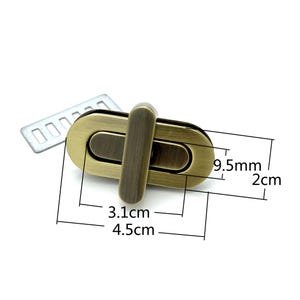 May include: A gold-toned metal clasp with a rectangular shape and a small, vertical bar in the center. The clasp measures 4.5 cm in length, 3.1 cm in width, and 2 cm in height.