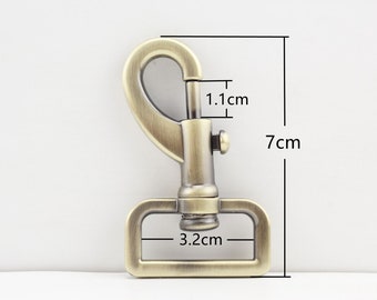 May include: Antique gold metal swivel hook with a 3.2 cm wide rectangular base and a 1.1 cm wide hook. The hook is 7 cm tall.
