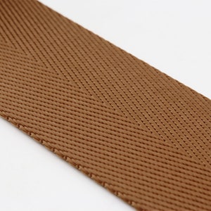 May include: Brown herringbone webbing ribbon. The ribbon is woven with a textured pattern.