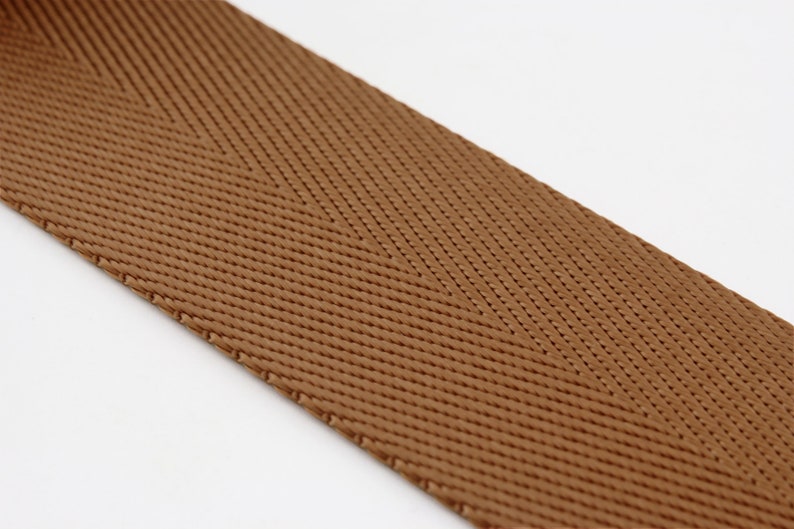 May include: Brown herringbone webbing ribbon. The ribbon is woven with a textured pattern.