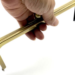May include: Gold-toned metal purse frame with a rounded top and two prongs at each end. The frame is designed to be used for creating a custom purse or bag.