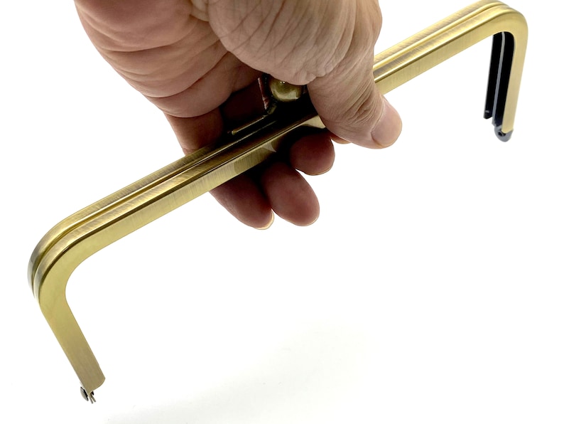 May include: Gold-toned metal purse frame with a rounded top and two prongs at each end. The frame is designed to be used for creating a custom purse or bag.