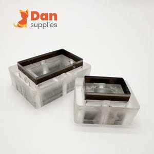 Puede incluir: Dos moldes rectangulares transparentes con marcos de metal marrón oscuro. Los moldes están apilados, con los marcos de metal en la parte superior. El logotipo "Dan supplies" está en la esquina superior izquierda, con un zorro de dibujos animados.