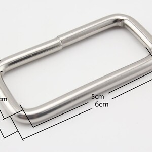 Pode incluir: Anel retangular de metal prateado com bordas arredondadas. O anel mede 6 cm de comprimento, 5 cm de largura e 2,2 cm de espessura.