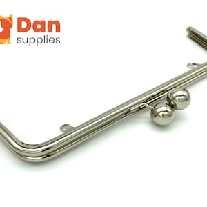 May include: A silver-toned purse frame with two round metal balls on the closure. The frame is made of two pieces of metal that are joined together at the top and bottom.