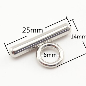 May include: Silver metal T-shaped connector with a 25 mm long bar and a 6 mm diameter ring. The bar is 14 mm wide.