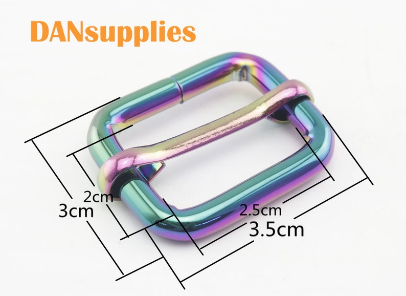 Op de afbeelding: Een regenboogkleurige, iriserende metalen gesp voor een band of riem. De gesp meet 2 cm bij 3,5 cm.