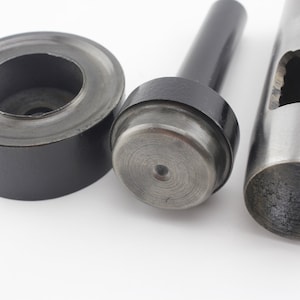 May include: A set of three metal tools for punching holes in leather. The tools are black and silver and have a circular shape.