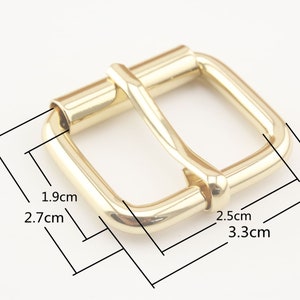 May include: Gold-toned metal buckle with a rectangular shape and rounded edges. The buckle measures 2.5 inches by 3.3 inches.