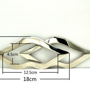 Op de afbeelding: Zilverkleurige metalen sculptuur met een golvend ontwerp. De sculptuur is 18 cm lang, 12,5 cm breed en 8 cm hoog.