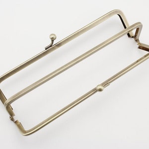 Op de afbeelding: Een gouden metalen tasframe met twee sluitingen. Het frame is open en klaar om te worden gebruikt voor een tas of portemonnee.