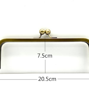 May include: A gold-toned metal purse frame with two round knobs at the top. The frame measures 7.5 inches by 20.5 inches.