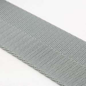 May include: A close-up of a gray woven webbing strap. The strap has a herringbone pattern and is made of a durable material.
