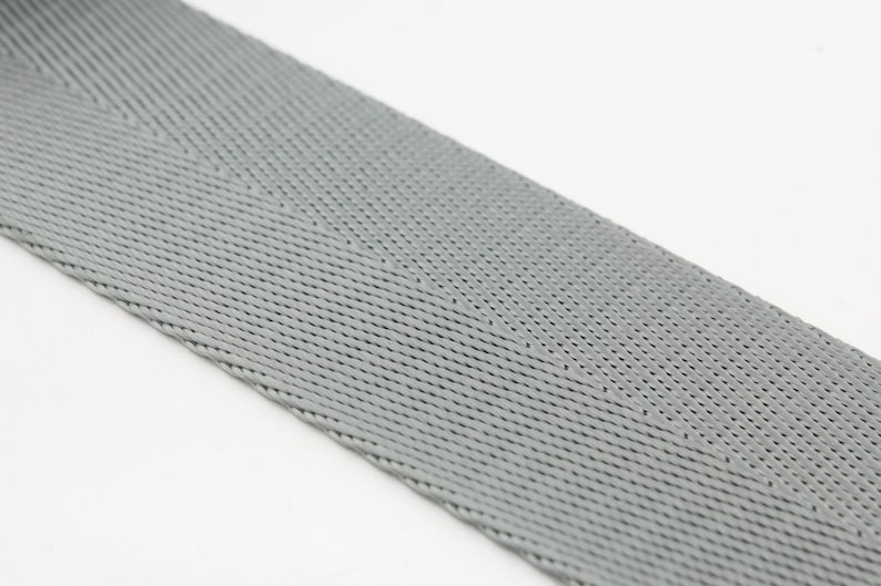 May include: A close-up of a gray woven webbing strap. The strap has a herringbone pattern and is made of a durable material.