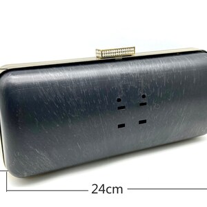Pu&ograve; includere: Una pochette nera con cornice in metallo dorato e chiusura con strass. La pochette misura 10 cm per 24 cm.