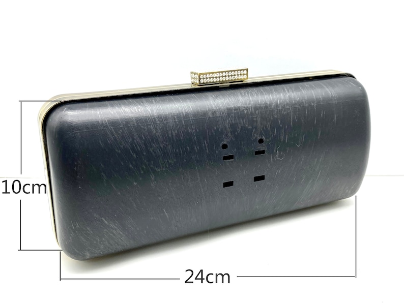 Pu&ograve; includere: Una pochette nera con cornice in metallo dorato e chiusura con strass. La pochette misura 10 cm per 24 cm.