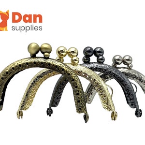 May include: Four ornate metal purse frames with decorative details and ball-shaped clasps. The frames are in gold, silver, and black.