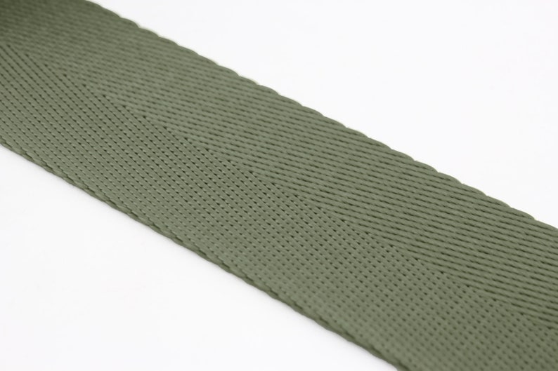 May include: A close-up of a green woven webbing strap. The strap has a herringbone pattern and is made of a durable material.