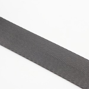 May include: A close-up of a gray woven webbing strap. The strap has a herringbone pattern and is made of a durable material.