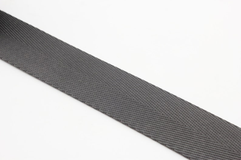 May include: A close-up of a gray woven webbing strap. The strap has a herringbone pattern and is made of a durable material.