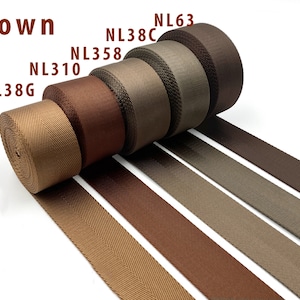 May include: Five rolls of brown nylon webbing tape arranged in a row, each labeled with codes NL38G, NL310, NL358, NL38C, and NL63. The textile straps feature a distinct herringbone weave pattern and vary in shades from light tan to dark chocolate brown.