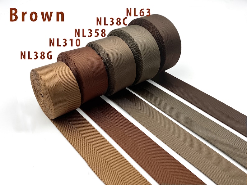 May include: Five rolls of brown nylon webbing tape arranged in a row, each labeled with codes NL38G, NL310, NL358, NL38C, and NL63. The textile straps feature a distinct herringbone weave pattern and vary in shades from light tan to dark chocolate brown.