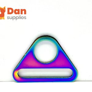 Pode incluir: Um anel triangular de metal iridescente arco-íris com um grande furo central e uma abertura retangular menor.