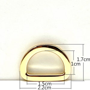 May include: Gold-toned metal D-ring with measurements: 1.7 cm x 1 cm x 2.2 cm.  The ring is a hardware component for bags, purses, and other accessories.