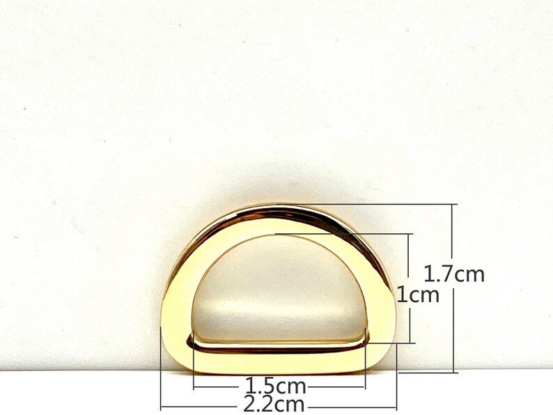 May include: Gold-toned metal D-ring with measurements: 1.7 cm x 1 cm x 2.2 cm.  The ring is a hardware component for bags, purses, and other accessories.