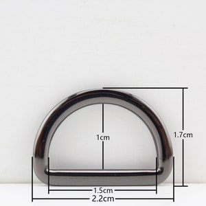 May include: A black metal D-ring with measurements: 1.7 cm tall, 1 cm wide, and 2.2 cm long.