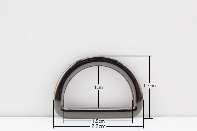 May include: A black metal D-ring with measurements: 1.7 cm tall, 1 cm wide, and 2.2 cm long.