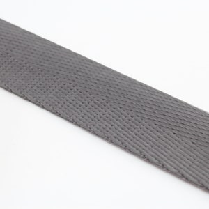 May include: A close-up of a gray woven webbing strap. The strap has a textured surface and is made of a durable material.