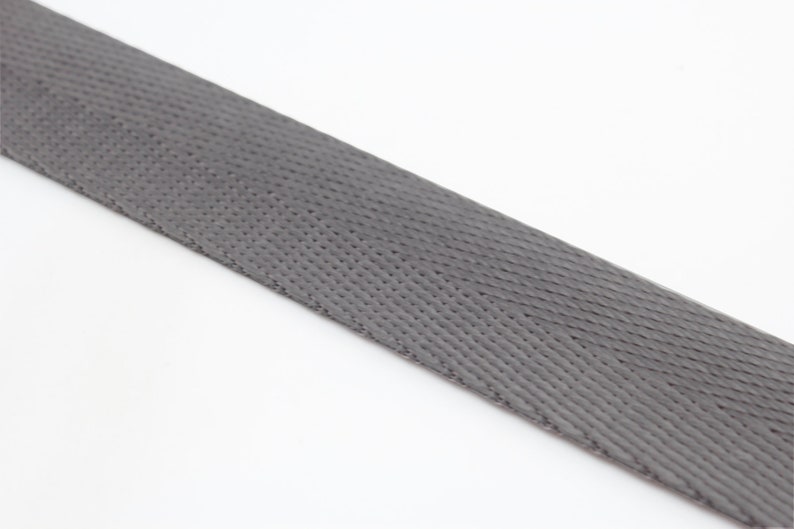 May include: A close-up of a gray woven webbing strap. The strap has a textured surface and is made of a durable material.