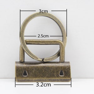 May include: Antique gold-toned metal key ring with a 3 cm diameter ring and a 3.2 cm long bar. The bar has two small holes on the top.