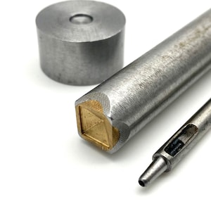 May include: A set of three metal tools for leather crafting. The tools include a round punch, a square punch, and a hollow punch. The punches are made of silver metal with a brass accent on the square punch.