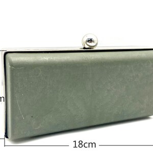 May include: A silver and green clutch purse with a silver ball clasp. The purse measures 8.5 inches by 18 inches.