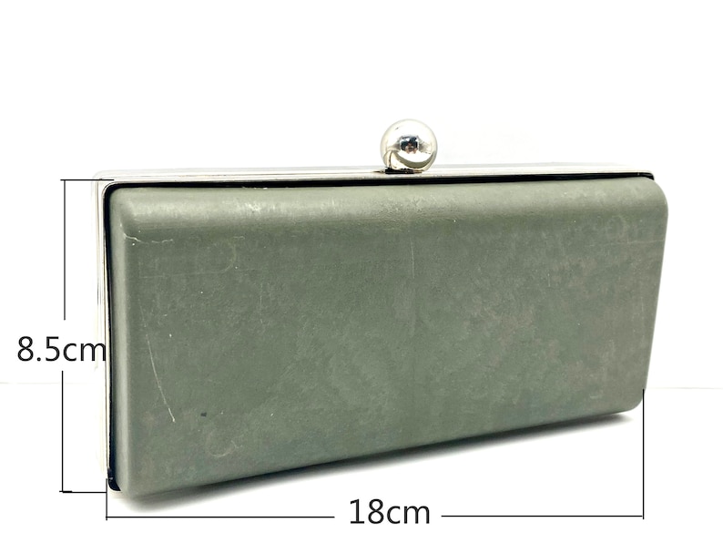 May include: A silver and green clutch purse with a silver ball clasp. The purse measures 8.5 inches by 18 inches.