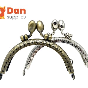 May include: Two ornate metal purse frames, one silver and one gold, with decorative floral patterns. The frames are designed to be used for creating purses or bags.