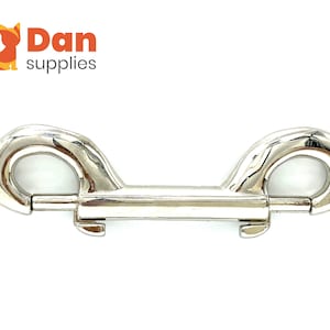 May include: A shiny, silver-colored double-ended bolt snap. The snap has two rounded eyelets and a central bar with a spring-loaded mechanism. The logo "Dan supplies" is in the upper left corner.